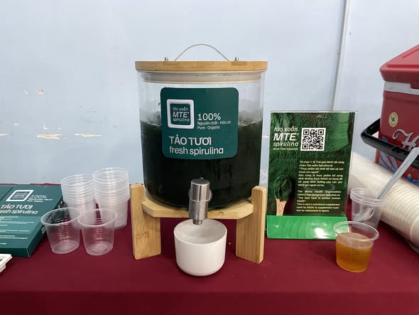Bình tảo xoắn tươi MTE Spirulina và ly dùng thử tại khu vực trưng bày sản phẩm.